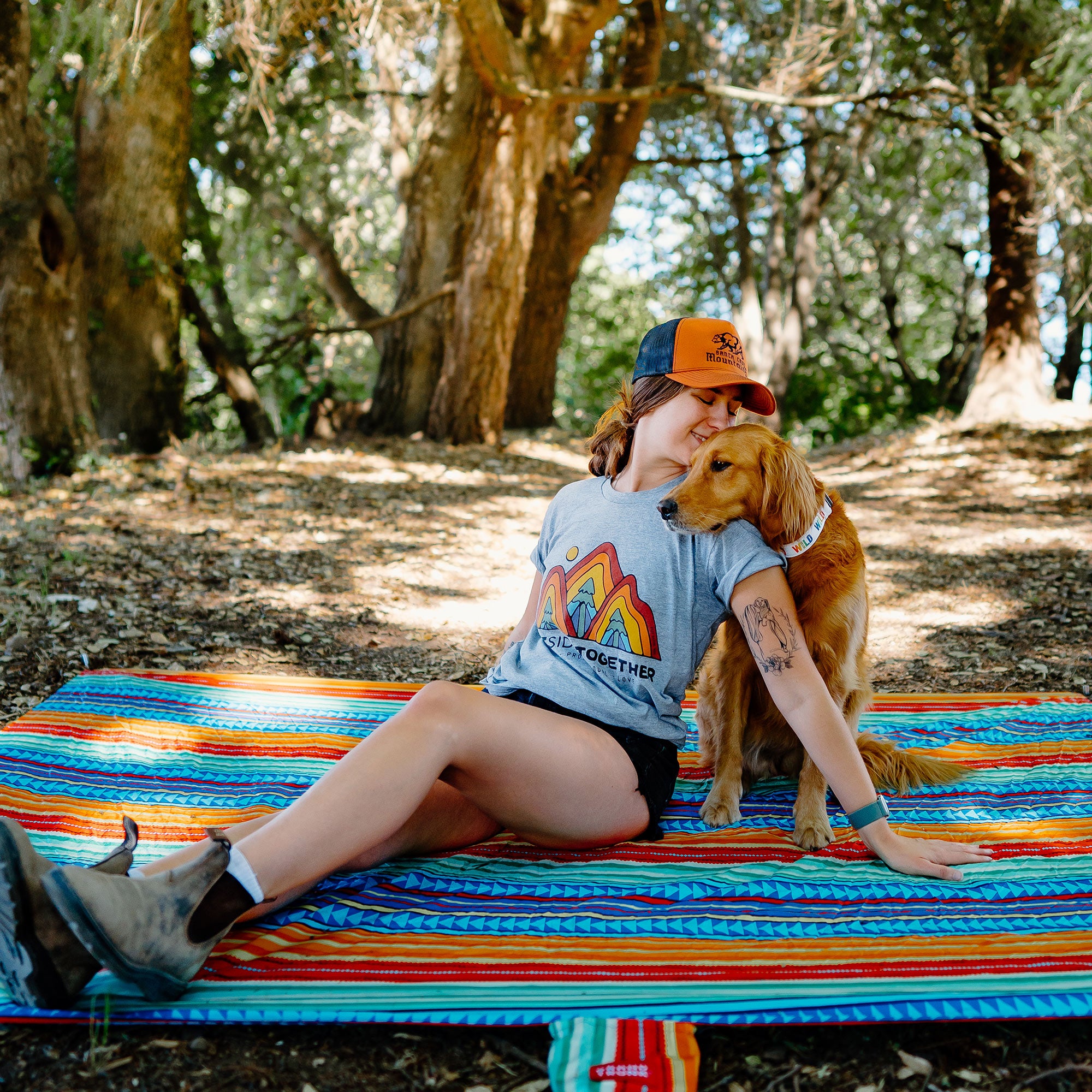 woman sits on adventure sheet in forest while snuggling dog