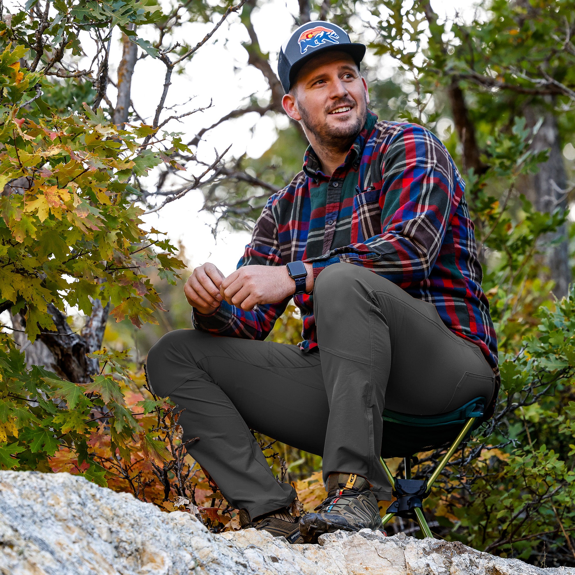 man sits on compass 360 stool smiling with fall foliage